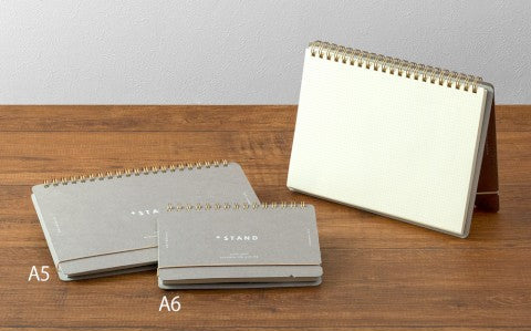 Three notebooks of different sizes on a wooden surface with a plain background
