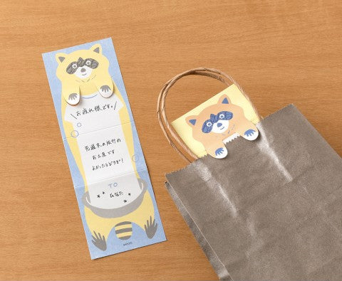 Bookmark with raccoon design and brown paper bag on wooden surface