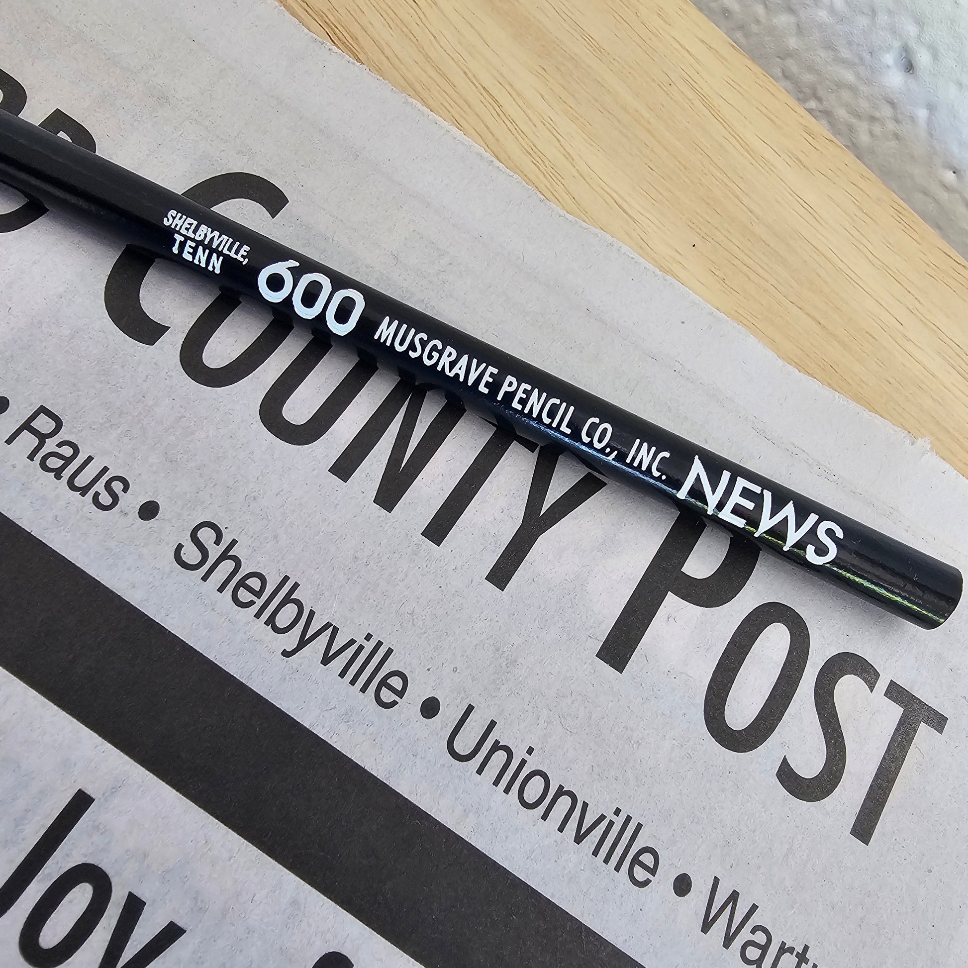 Black pencil on a newspaper with visible text