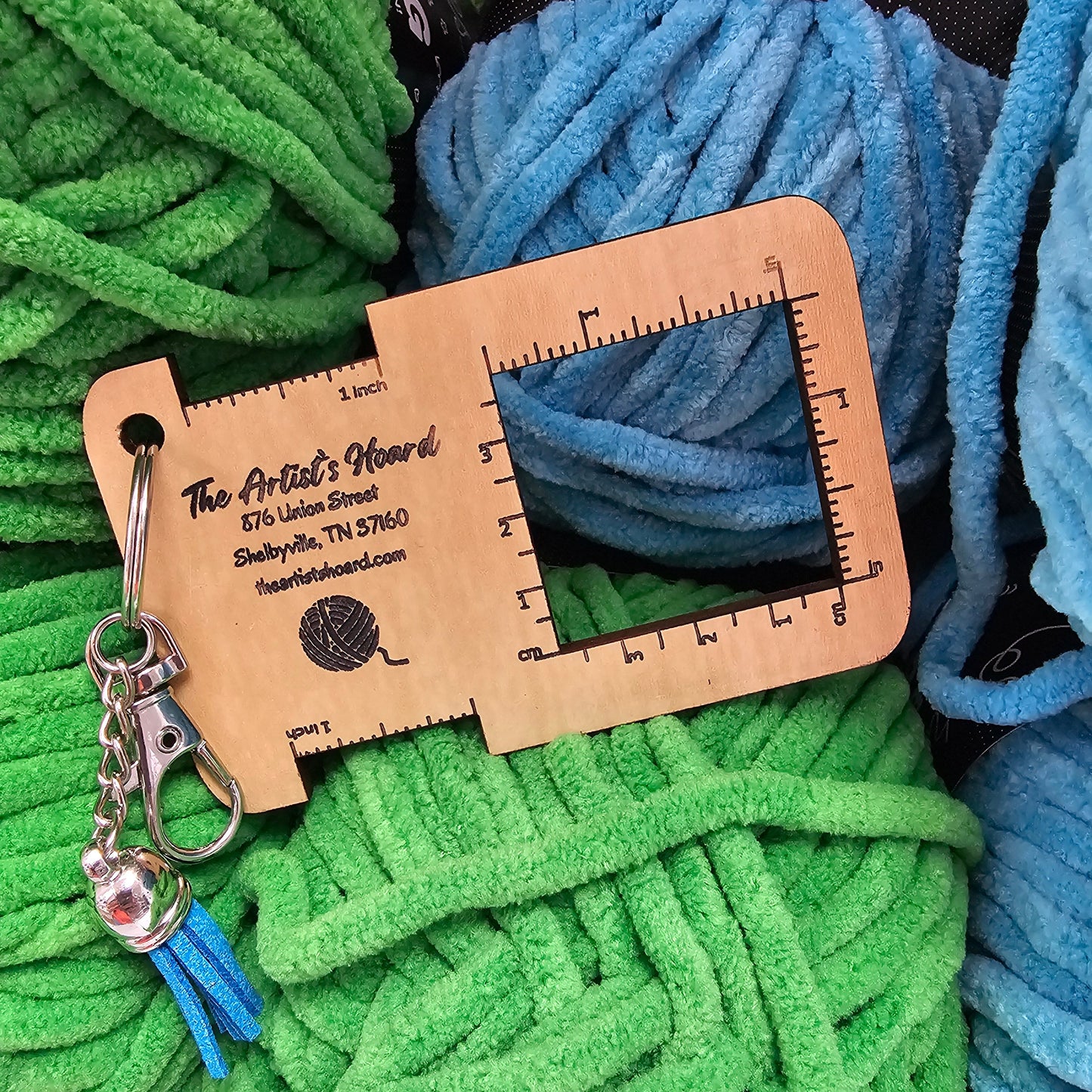 Yarn with a wooden gauge tool on top, surrounded by green and blue yarn.