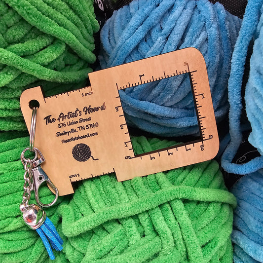 Yarn with a wooden gauge tool on top, surrounded by green and blue yarn.